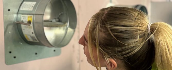 Female engineer closely inspecting a fire damper inside a ceiling void