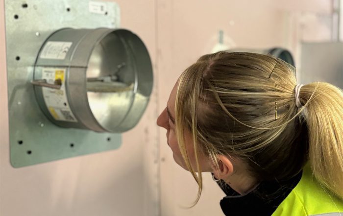 Female engineer closely inspecting a fire damper inside a ceiling void